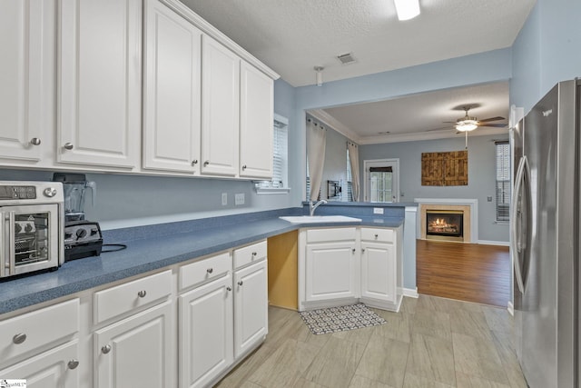 kitchen featuring freestanding refrigerator, a sink, a lit fireplace, a peninsula, and white cabinetry