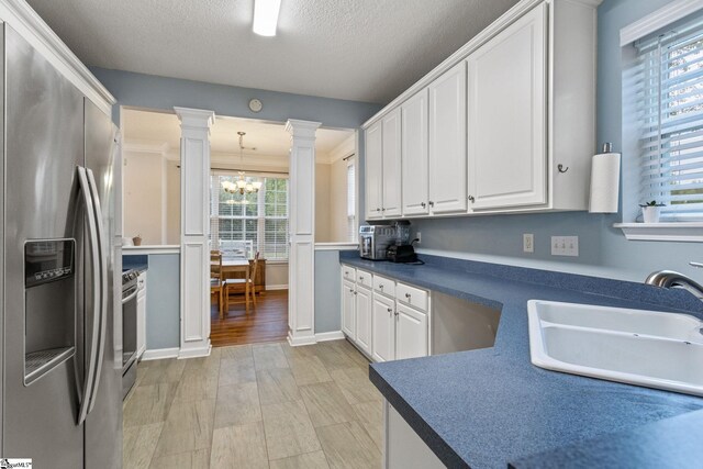 kitchen with appliances with stainless steel finishes, decorative columns, a sink, a chandelier, and white cabinetry