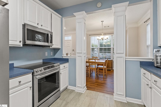 kitchen featuring stainless steel appliances, decorative columns, dark countertops, white cabinetry, and crown molding