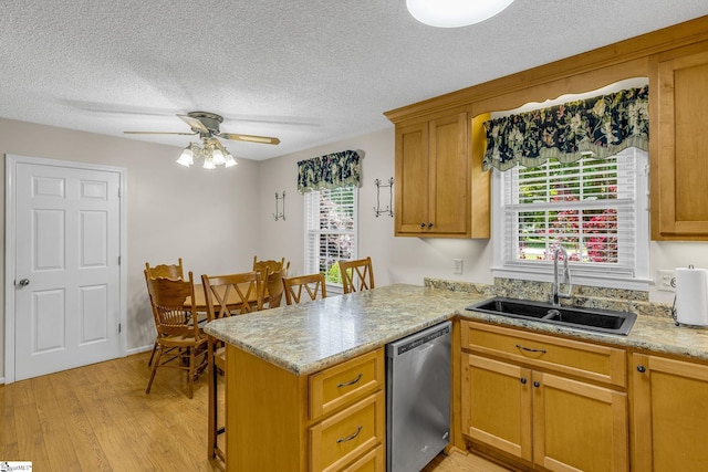 kitchen featuring stainless steel dishwasher, a sink, a textured ceiling, a peninsula, and light wood-style flooring