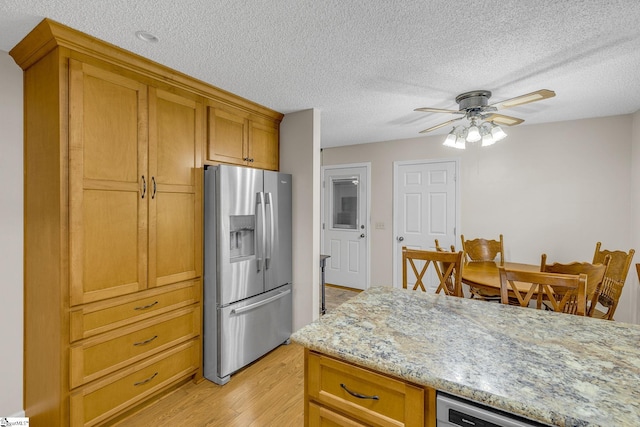 kitchen featuring stainless steel refrigerator with ice dispenser, light wood-style flooring, ceiling fan, brown cabinetry, and a textured ceiling