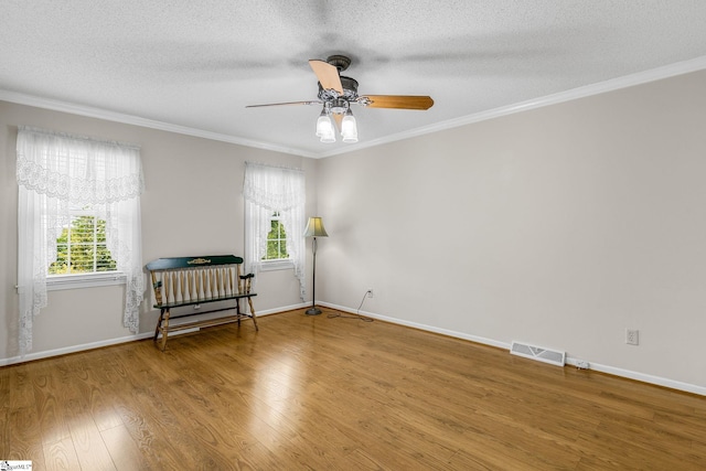 empty room featuring wood finished floors, ornamental molding, a ceiling fan, a textured ceiling, and baseboards