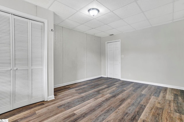 unfurnished bedroom with wood finished floors, baseboards, a drop ceiling, and a closet