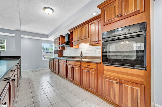 kitchen featuring black oven, wall chimney range hood, a textured ceiling, backsplash, and dark countertops