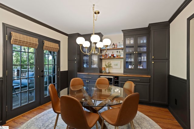 dining space with wainscoting, a dry bar, a chandelier, wood finished floors, and crown molding