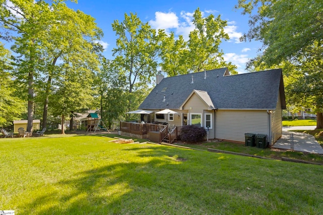 back of property with a playground, a chimney, a wooden deck, a lawn, and roof with shingles