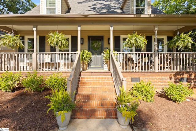 entrance to property with a porch and a shingled roof