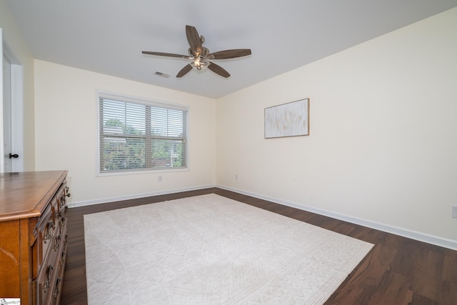 empty room with dark wood finished floors, a ceiling fan, and baseboards