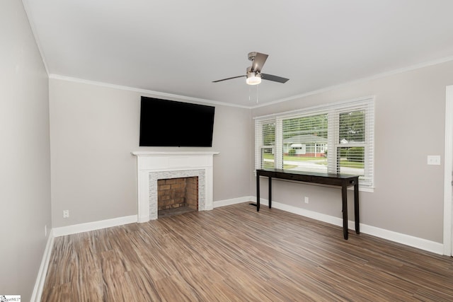unfurnished living room with ceiling fan, wood finished floors, ornamental molding, baseboards, and a fireplace