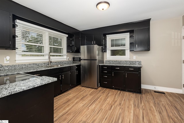 kitchen with stainless steel appliances, dark cabinetry, a sink, and light wood-type flooring