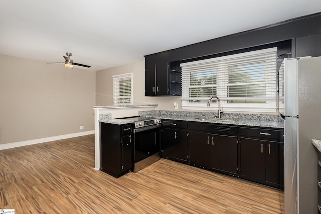 kitchen featuring appliances with stainless steel finishes, a sink, dark cabinets, light wood-type flooring, and a ceiling fan