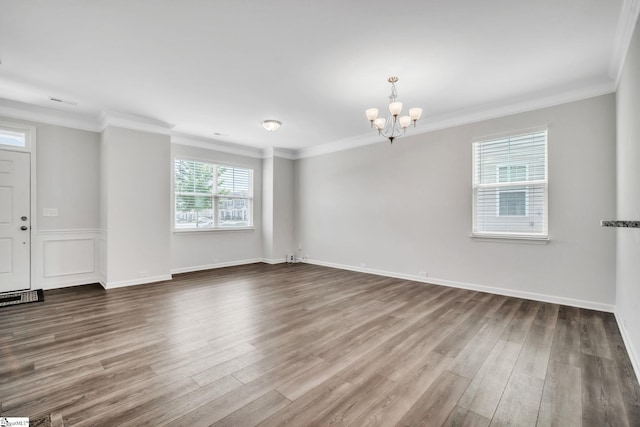 spare room with a chandelier, wood finished floors, ornamental molding, and baseboards
