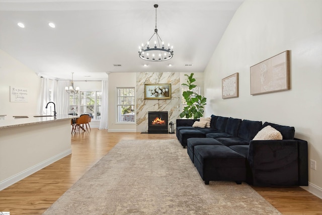 living area featuring a chandelier, light wood finished floors, a premium fireplace, baseboards, and recessed lighting