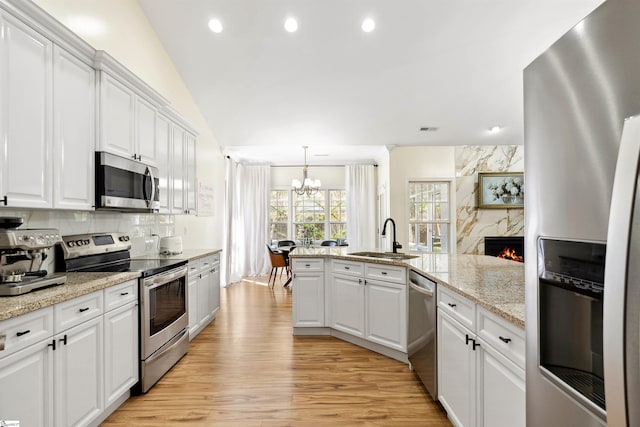 kitchen featuring appliances with stainless steel finishes, a sink, a chandelier, white cabinets, and light wood finished floors