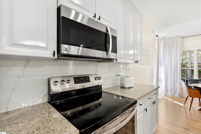 kitchen with stainless steel appliances, white cabinets, backsplash, light wood-type flooring, and light stone counters