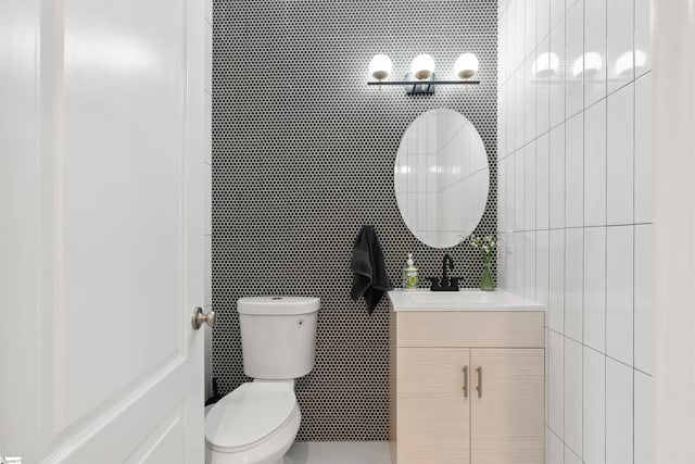 half bath with tile walls, toilet, and vanity