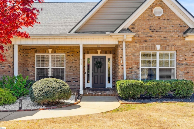 view of exterior entry featuring brick siding, roof with shingles, and covered porch