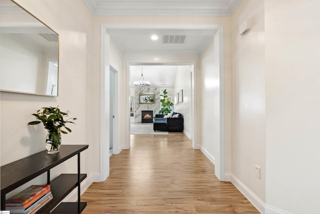corridor with light wood-style flooring, crown molding, baseboards, and a chandelier