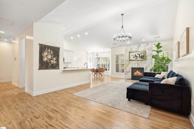 living room with a chandelier, vaulted ceiling, a fireplace, light wood-style flooring, and baseboards