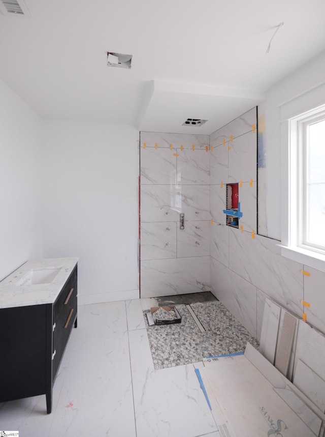 full bath with tiled shower, marble finish flooring, and vanity