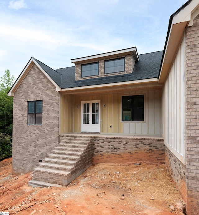 view of exterior entry featuring board and batten siding, a shingled roof, and brick siding