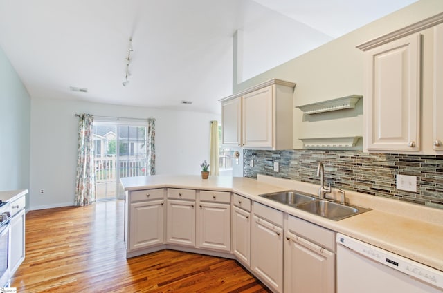 kitchen with dishwasher, a sink, a peninsula, light wood-type flooring, and backsplash