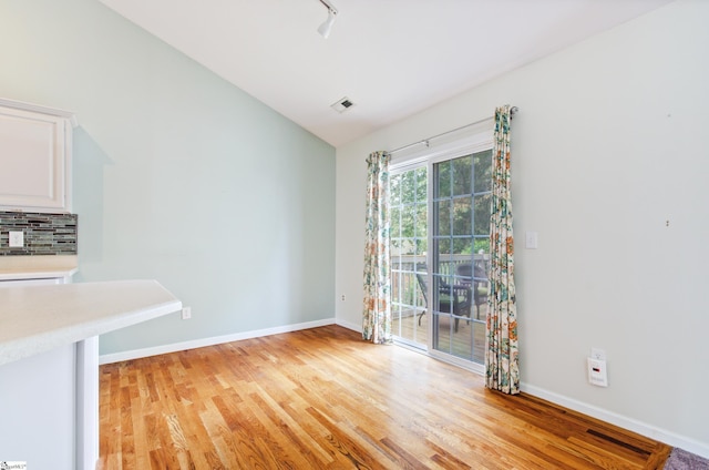 unfurnished dining area featuring light wood-style flooring, vaulted ceiling, and baseboards