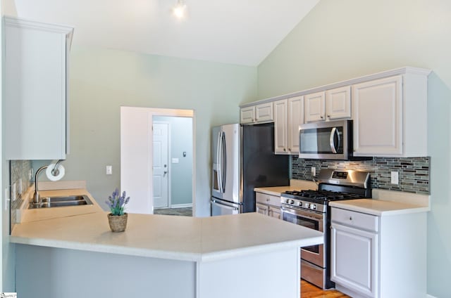 kitchen featuring appliances with stainless steel finishes, a sink, backsplash, lofted ceiling, and light countertops