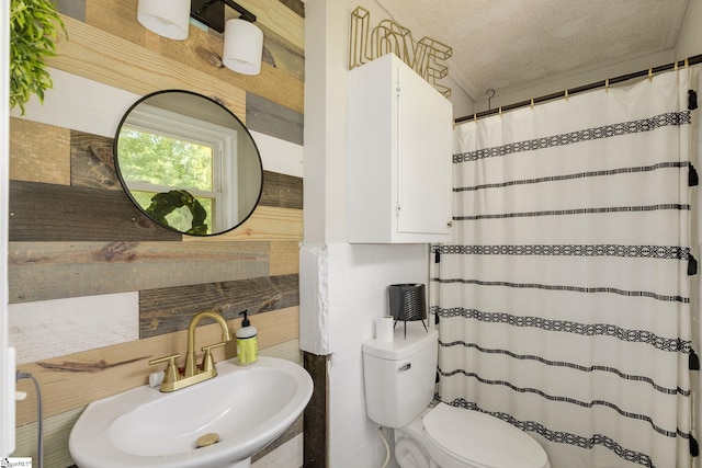 full bath with a sink, toilet, a shower with curtain, a textured ceiling, and tile walls