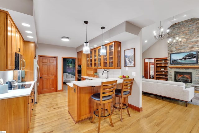 kitchen with appliances with stainless steel finishes, light wood-type flooring, glass insert cabinets, a peninsula, and brown cabinetry