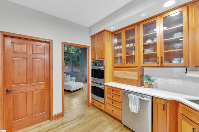 kitchen with stainless steel appliances, light wood-style floors, light countertops, and glass insert cabinets