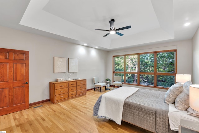 bedroom featuring a tray ceiling, light wood-type flooring, baseboards, recessed lighting, and ceiling fan