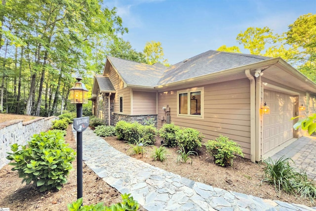 view of side of home with a garage, roof with shingles, and driveway
