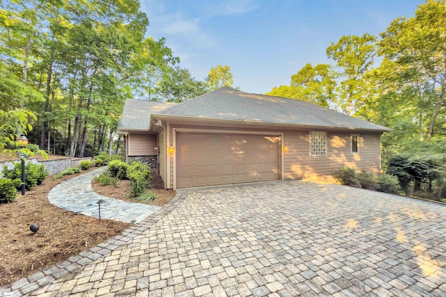 view of side of home featuring a garage, decorative driveway, and roof with shingles