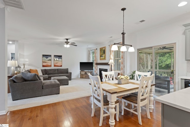 dining room with ceiling fan, light wood-type flooring, a fireplace, baseboards, and ornamental molding