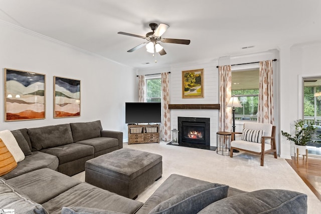 living room featuring ornamental molding, plenty of natural light, a ceiling fan, baseboards, and a large fireplace