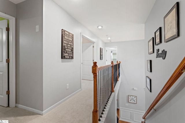 hallway with an upstairs landing, light colored carpet, and baseboards