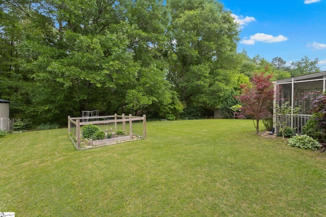 view of grassy yard featuring a vegetable garden and a sunroom