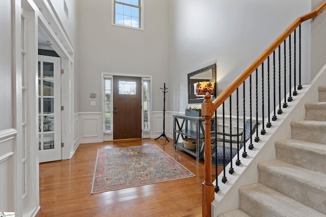 foyer entrance featuring healthy amount of natural light, stairs, a towering ceiling, a decorative wall, and wood finished floors