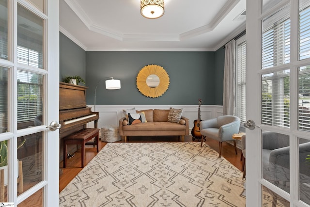 living area with wood finished floors, a raised ceiling, ornamental molding, wainscoting, and a decorative wall