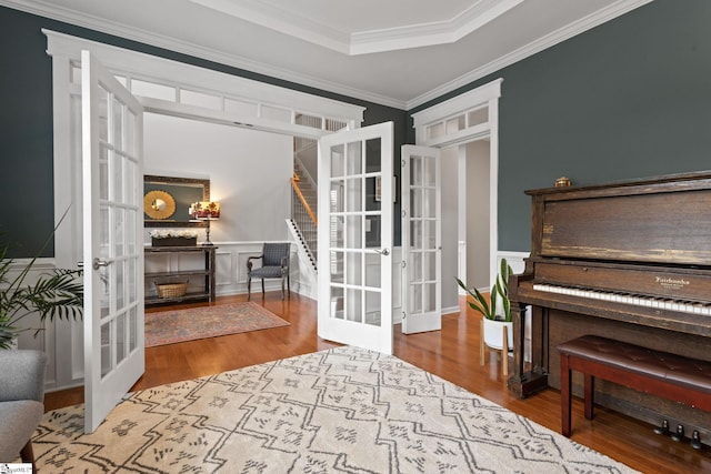 sitting room featuring french doors, wood finished floors, ornamental molding, and stairs