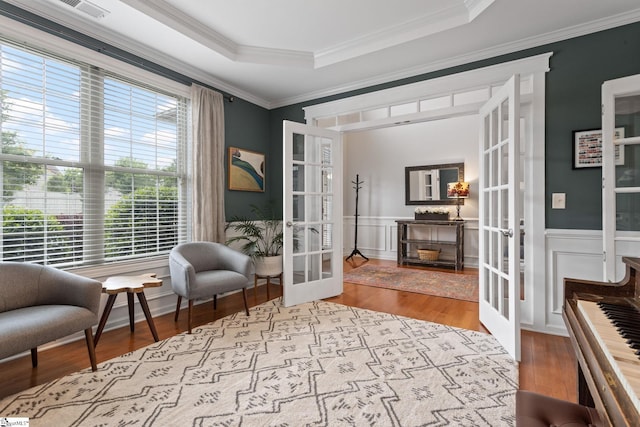living area with french doors, a raised ceiling, wood finished floors, wainscoting, and crown molding