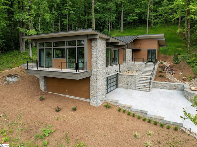 back of property with stone siding, a garage, stairway, a forest view, and a balcony