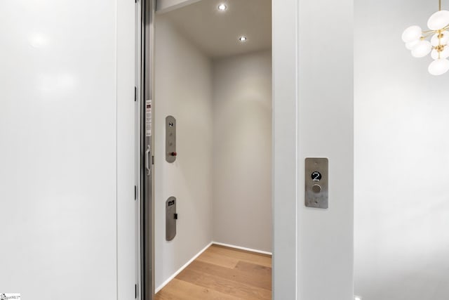 laundry room featuring elevator, light wood-type flooring, recessed lighting, a chandelier, and baseboards