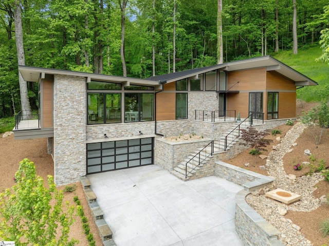 view of front of house featuring stone siding, a garage, concrete driveway, and stairs