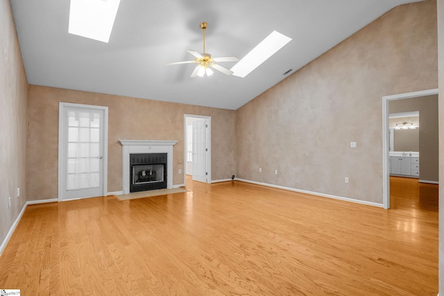 unfurnished living room with a skylight, light wood-style floors, a fireplace with flush hearth, and high vaulted ceiling