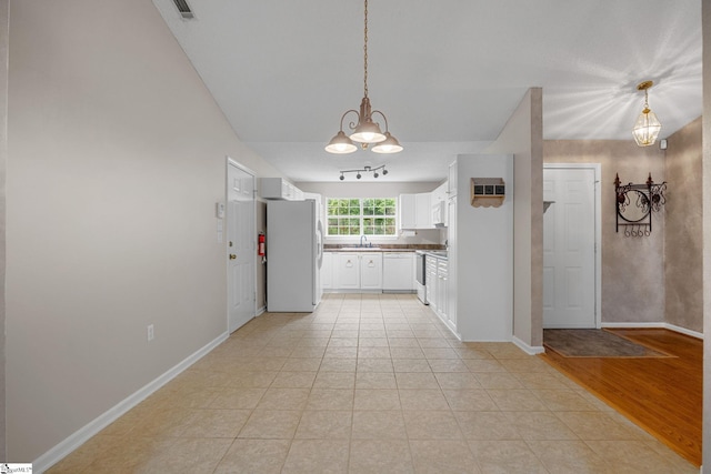 kitchen with freestanding refrigerator, a sink, white cabinets, decorative light fixtures, and baseboards
