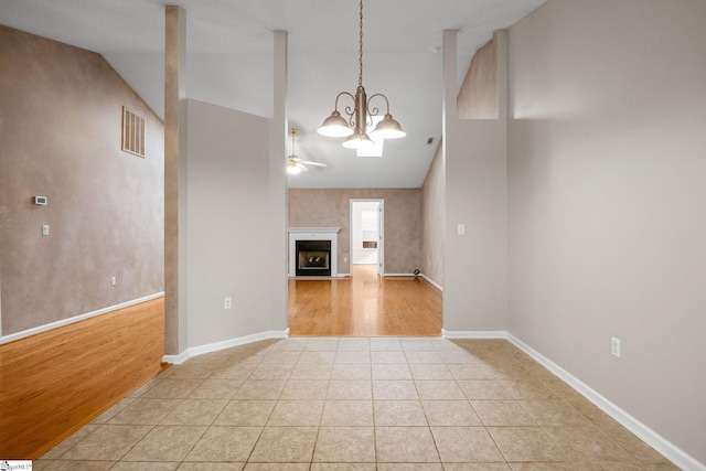 unfurnished living room with a chandelier, high vaulted ceiling, ceiling fan, light tile patterned floors, and baseboards