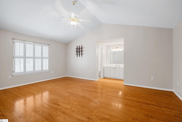 unfurnished bedroom with vaulted ceiling, light wood-style floors, a sink, baseboards, and connected bathroom