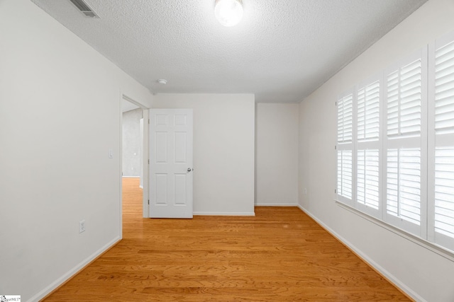 spare room with light wood finished floors, a textured ceiling, and baseboards
